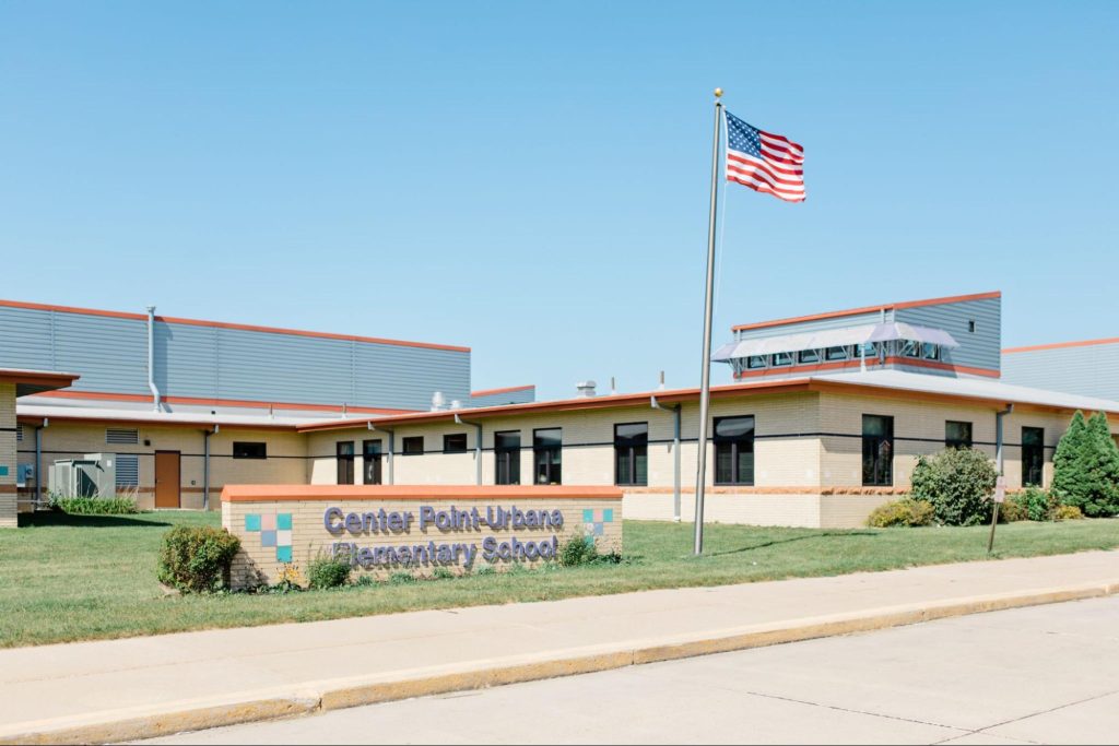 Exterior of a school building with an American flag and a sign that says "Center Point-Urbana Elementary School" in the foreground