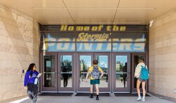 High school students walk in and out of the high school entrance. A banner that says 