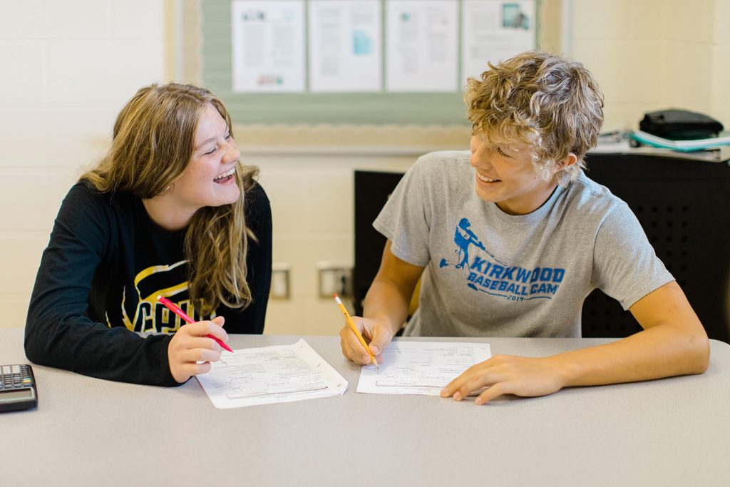 Two high school students smile and laugh with each other while working on an assignment