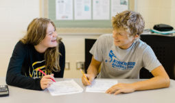 Two high school students smile and laugh with each other while working on an assignment