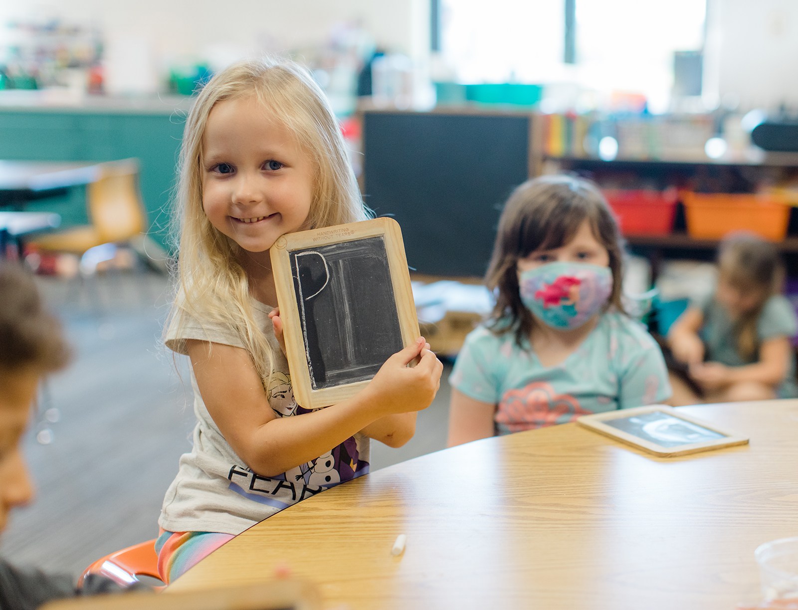 Preschool student shows off the letter P written on a handheld chalkboard