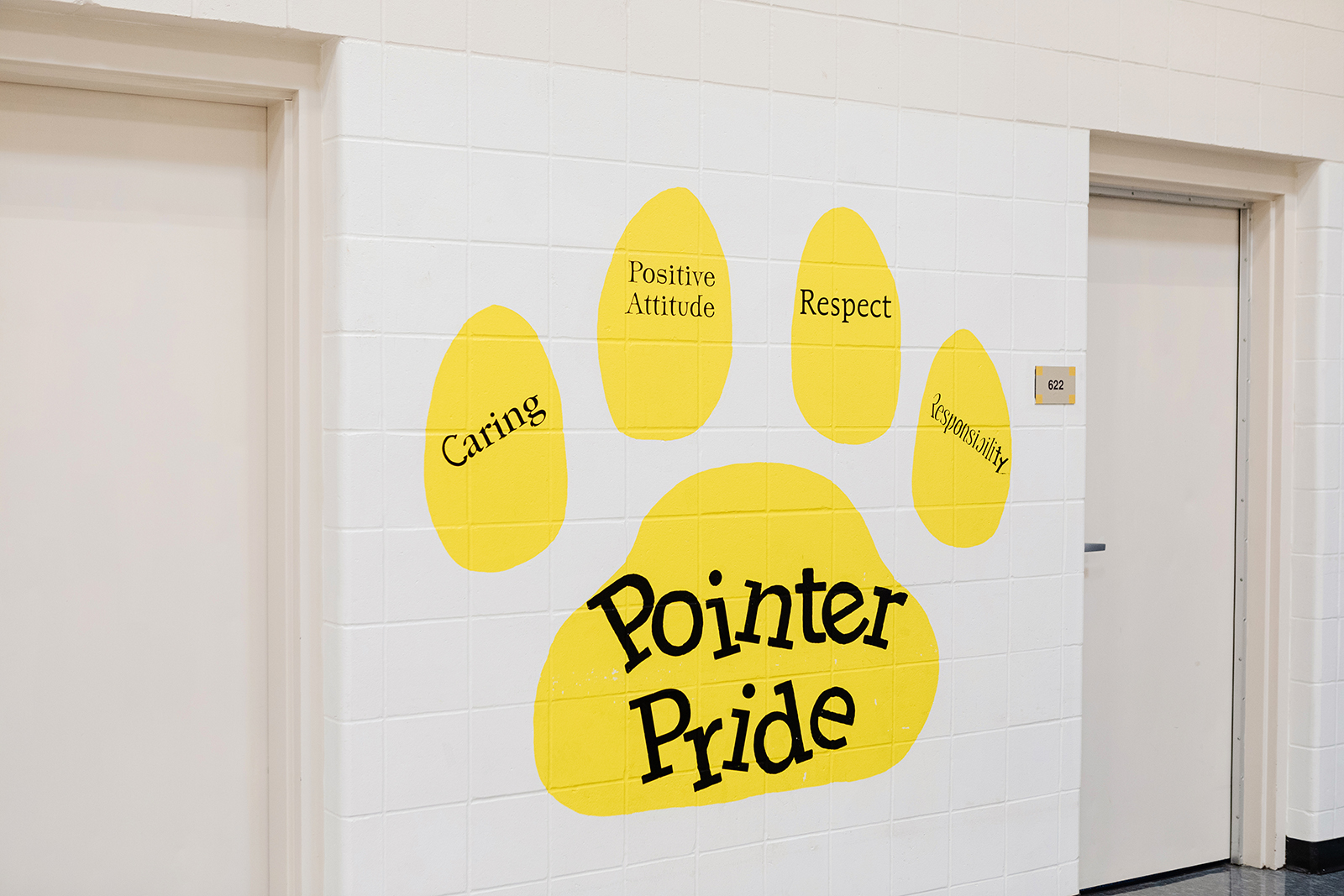 Yellow paw print painted on a wall that has "Pointer Pride" in the center with