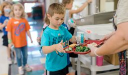 A lunch room staff person hands a tray of food to an elementary student