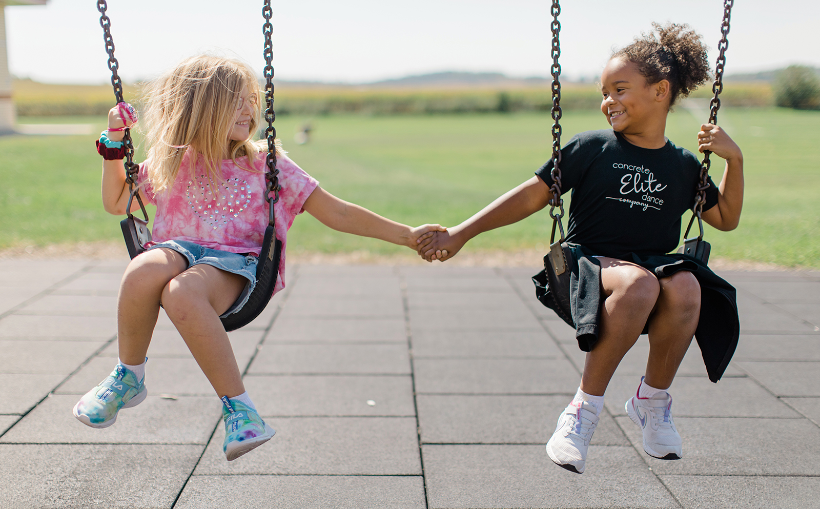 Two students hold hands while on a swingset at recess