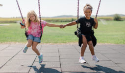 Two elementary age girls hold hands while on a swing set